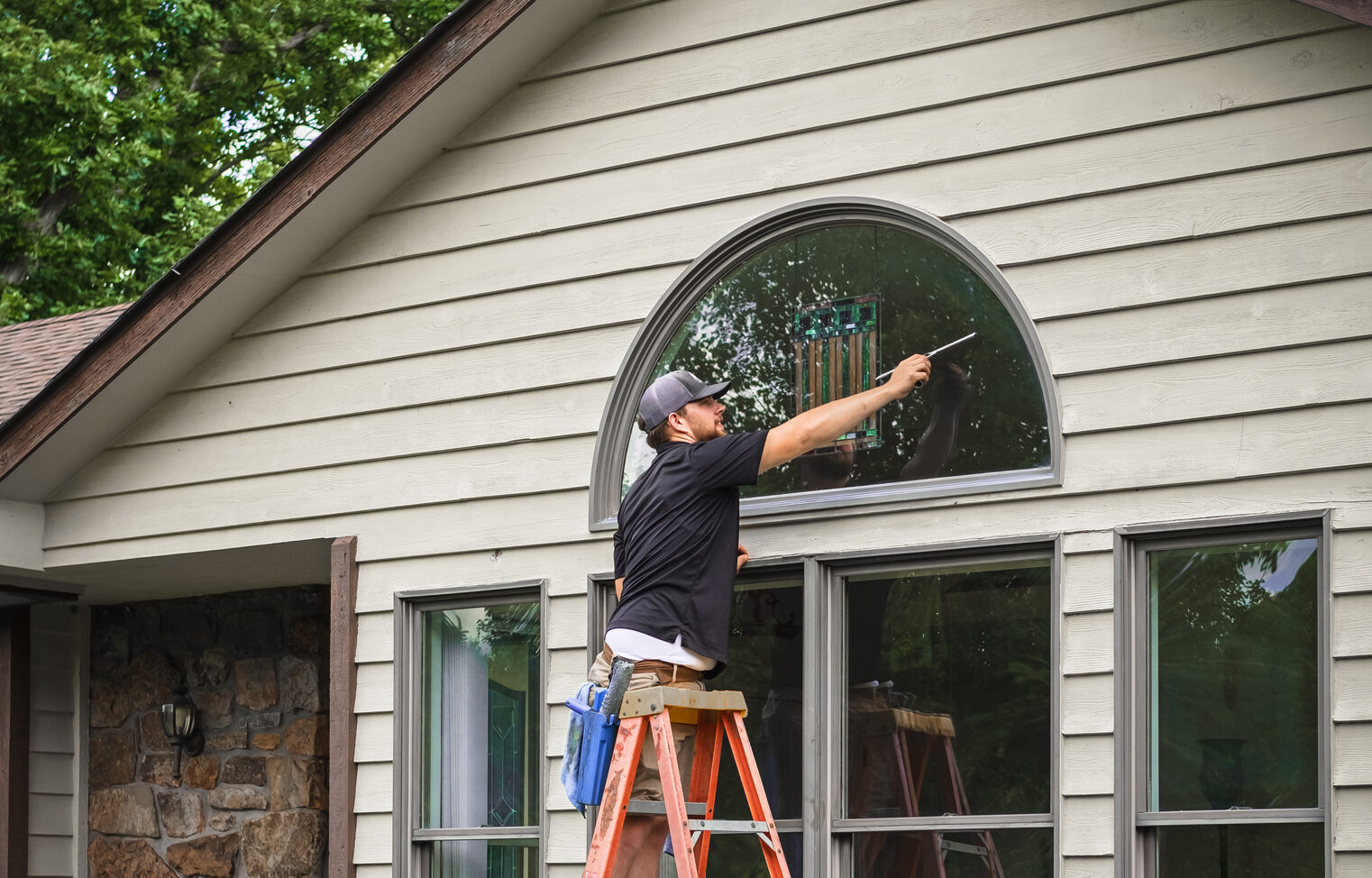 Young man standing on ladder washing outside windows of Midwestern house